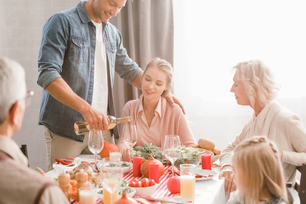 Family members sitting at table and smiling father pouring wine in Thanksgiving day — Stock Photo