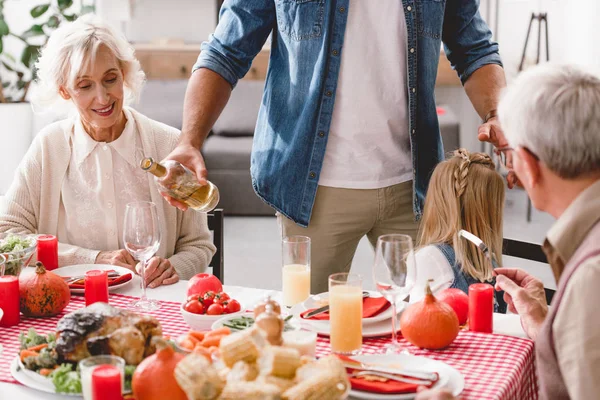 Abgeschnittene Ansicht von Familienmitgliedern, die am Tisch sitzen und Vater Wein zum Dank einschenkt — Stockfoto