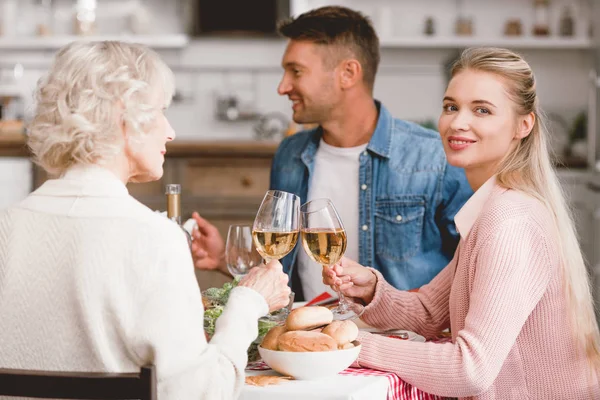 Miembros de la familia sonrientes sentados a la mesa y tintineando con copas de vino en el día de Acción de Gracias - foto de stock