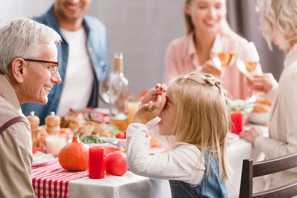 Селективное внимание улыбающегося дедушки, играющего с внучкой в День Благодарения — стоковое фото