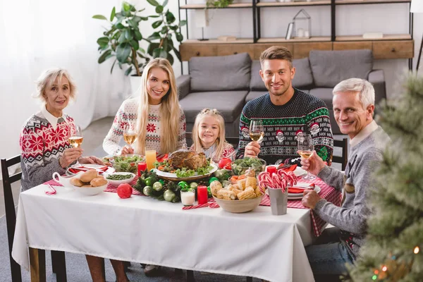 Familiari sorridenti seduti a tavola e che tengono bicchieri di vino a Natale — Foto stock