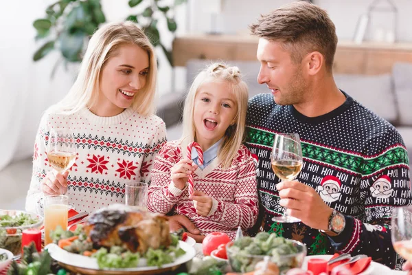 Улыбающиеся члены семьи сидят за столом и держат бокалы с вином на Рождество — стоковое фото