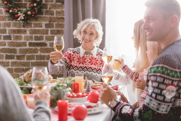 Foyer sélectif des membres de la famille assis à la table et tenant des verres à vin à Noël — Photo de stock