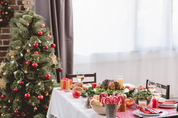 Plato con sabroso pavo, maíz, bastones de caramelo, velas, copas de regalo y vino en la mesa y el árbol de Navidad - foto de stock