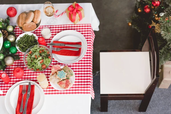 Vista superior de platos, ensalada, espárragos, copa de vino, velas y regalo en la mesa en Navidad - foto de stock