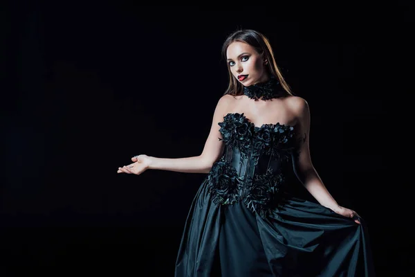 Страшная девушка-вампир в черно-готическом платье указывая рукой, изолированной на черном — стоковое фото