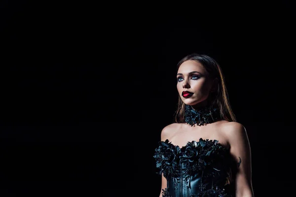 Espeluznante chica vampiro en vestido gótico negro mirando hacia otro lado aislado en negro - foto de stock