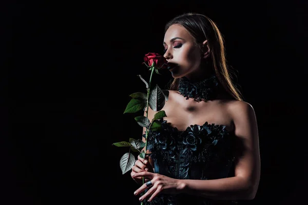 Страшна дівчина вампіра в чорній готичній сукні, що тримає червону троянду ізольовано на чорному — стокове фото