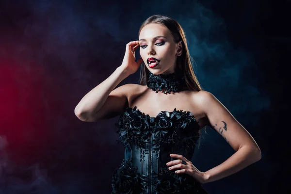 Scary vampire girl with fangs in black gothic dress on black background with smoke — Stock Photo