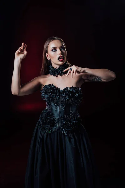 Scary vampire girl with fangs in black gothic dress on black background — Stock Photo