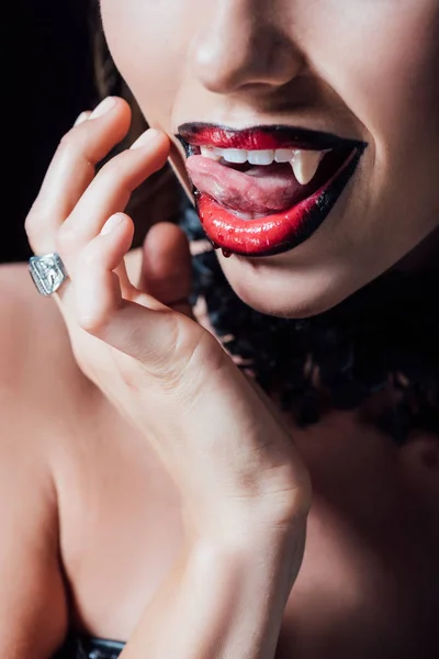 Recortado vista de miedo vampiro chica lamiendo colmillos aislado en negro - foto de stock