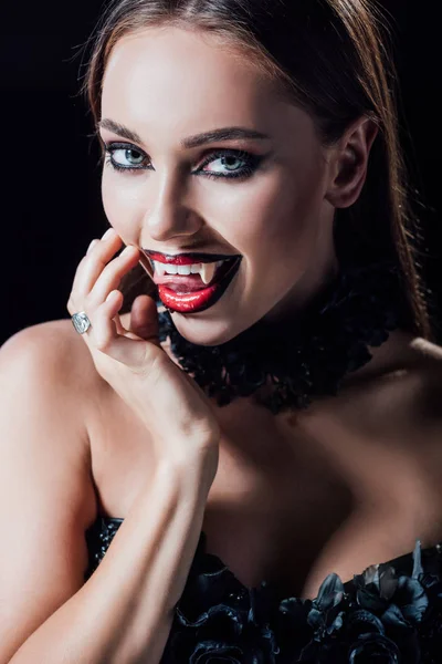 Страшная девушка-вампир показывает клыки в черно-готическом платье, изолированном на черном — стоковое фото