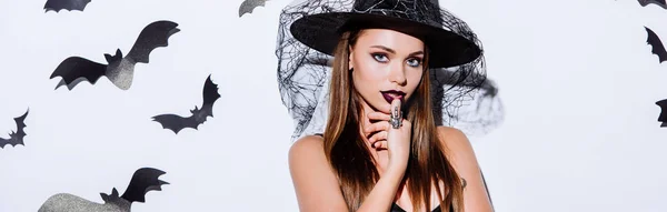 Plano panorámico de chica en traje de Halloween bruja negro cerca de la pared blanca con murciélagos decorativos - foto de stock