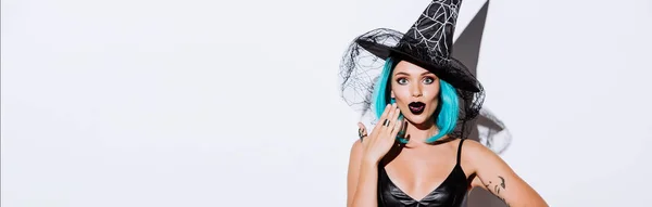 Панорамный снимок шокированной девушки в костюме черной ведьмы на Хэллоуин с голубыми волосами на белом фоне — стоковое фото