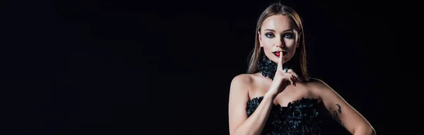 Panoramic shot of scary vampire girl in black gothic dress showing shh sign isolated on black — Stock Photo