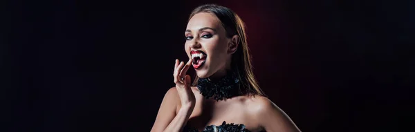 Panoramic shot of scary vampire girl showing fangs in black gothic dress isolated on black — Stock Photo