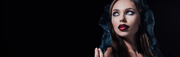 Tiro panorâmico de assustador vampiro menina em vestido gótico preto e véu olhando para longe isolado em preto — Fotografia de Stock