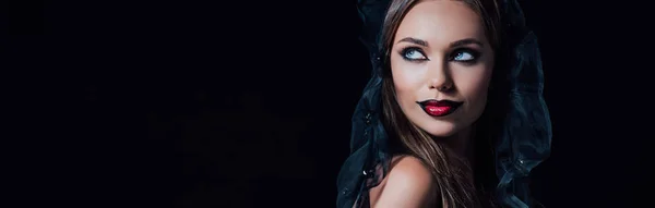 Панорамный снимок страшной девушки-вампира в черно-готическом платье и вуали, смотрящей в сторону, изолированной от черного — стоковое фото