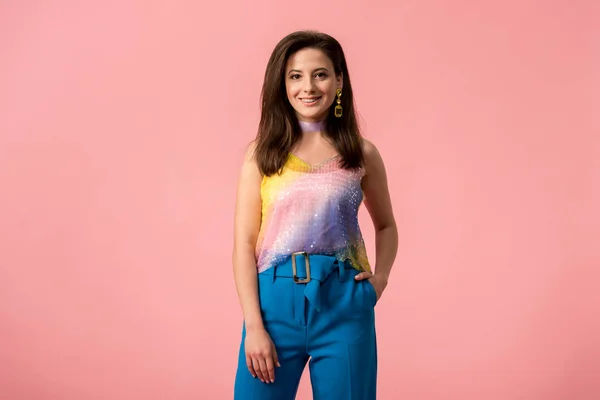 Sonriente joven y elegante chica disco con la mano en el bolsillo aislado en rosa - foto de stock