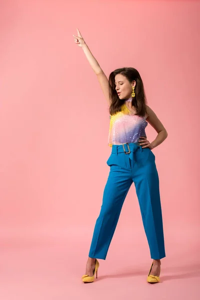 Vista completa de la excitada joven y elegante chica disco bailando con la mano en el aire en rosa - foto de stock