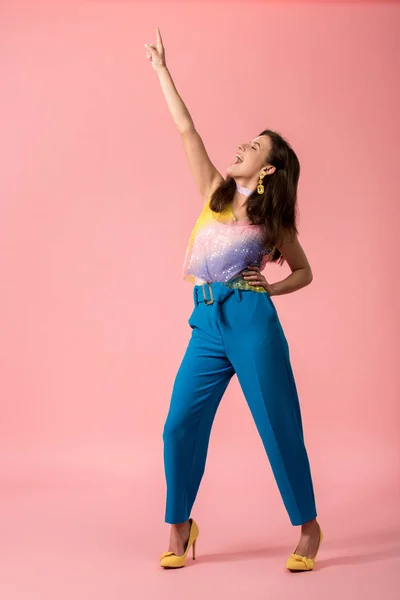 Vista completa de la excitada joven y elegante chica disco bailando con la mano en el aire en rosa - foto de stock