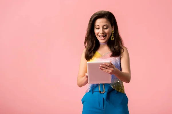 Excited young stylish disco girl holding digital tablet isolated on pink — Stock Photo