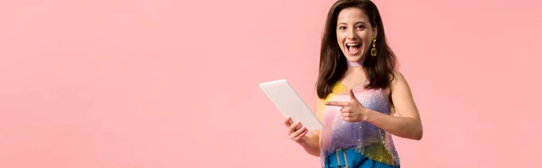 Plano panorámico de excitado joven y elegante chica disco apuntando con el dedo a la tableta digital aislado en rosa - foto de stock