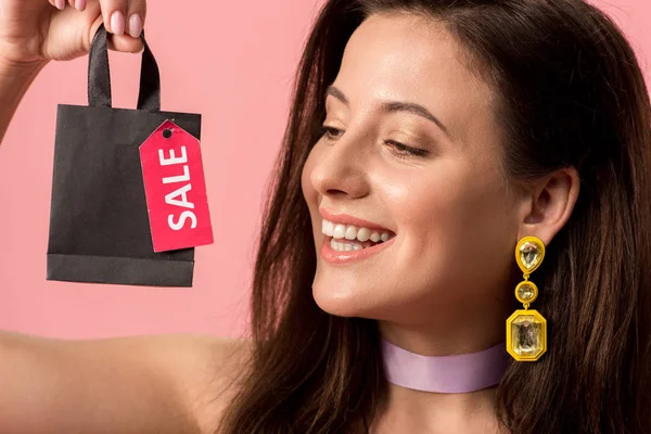 Chica disco con estilo feliz celebración de la bolsa de compras con la venta de letras en la etiqueta aislado en rosa - foto de stock