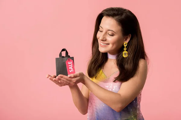 Sorridente elegante discoteca menina segurando saco de compras com letras venda no rótulo isolado em rosa — Fotografia de Stock
