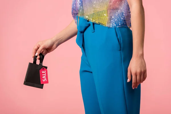 Cropped view of stylish disco girl holding shopping bag with sale lettering on label isolated on pink — Stock Photo