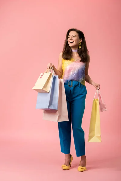 Full length view of happy stylish disco girl holding shopping bags on pink — Stock Photo