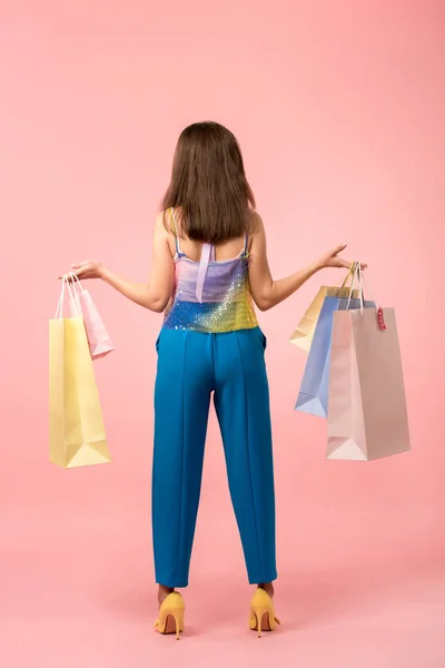 Вид сзади счастливой стильной девушки на дискотеке, держащей сумки с покупками на розовом фоне — стоковое фото