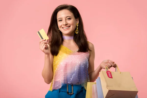 Menina disco elegante feliz segurando sacos de compras e cartão de crédito isolado em rosa — Fotografia de Stock