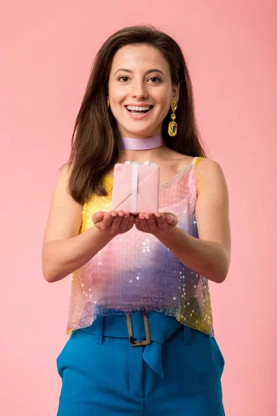 Feliz joven con estilo disco chica sosteniendo caja de regalo aislado en rosa - foto de stock