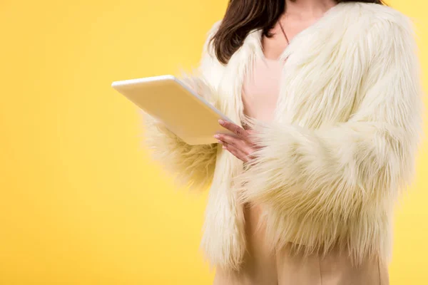 Vista ritagliata di elegante ragazza in pelliccia sintetica giacca utilizzando tablet digitale isolato su giallo — Foto stock