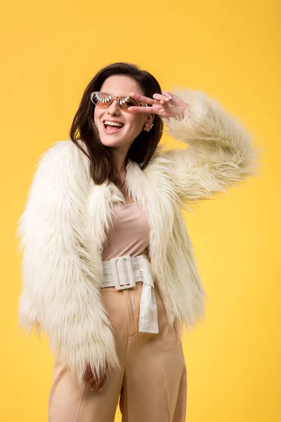 Excitada chica de fiesta en chaqueta de piel sintética y gafas de sol bailando aislado en amarillo - foto de stock