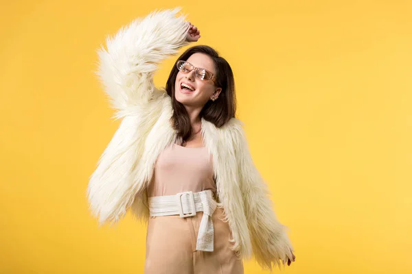 Excited party girl in faux fur jacket and sunglasses dancing isolated on yellow — Stock Photo