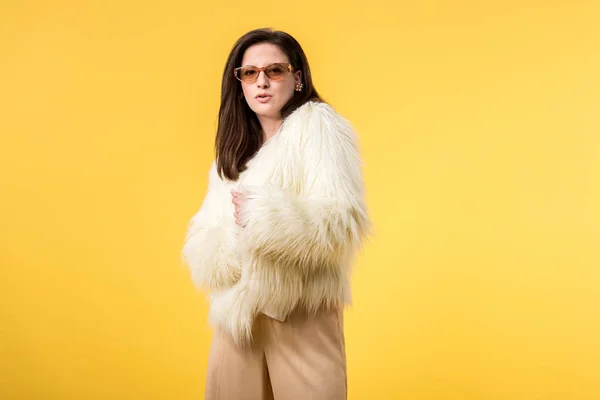 Elegante ragazza partito in giacca di pelliccia sintetica e occhiali da sole isolati su giallo — Foto stock