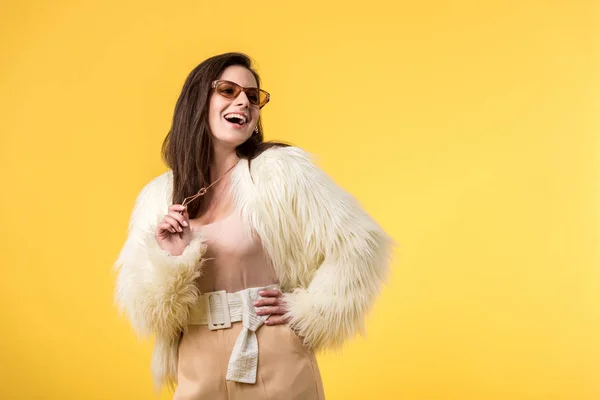 Excitada chica de fiesta en chaqueta de piel sintética y gafas de sol aisladas en amarillo - foto de stock