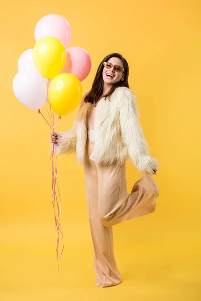 Heureuse fête fille en fausse fourrure veste et lunettes de soleil posant avec des ballons — Photo de stock