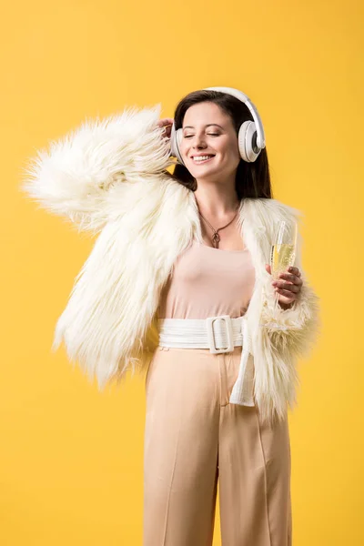 Chica sonriente en chaqueta de piel sintética escuchando música en auriculares aislados en amarillo - foto de stock