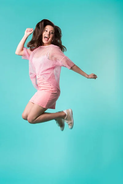 Збуджена дівчина з відкритим ротом в рожевому вбранні стрибає ізольовано на бірюзовому — стокове фото