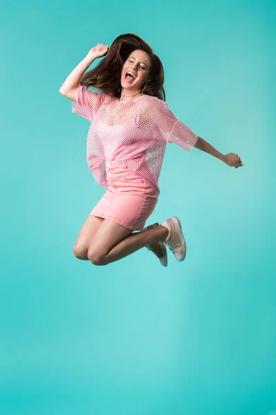 Збуджена дівчина з відкритим ротом в рожевому вбранні стрибає ізольовано на бірюзовому — стокове фото