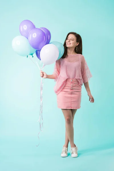 Улыбающаяся девушка в розовом наряде держит воздушные шары на бирюзовом фоне — стоковое фото