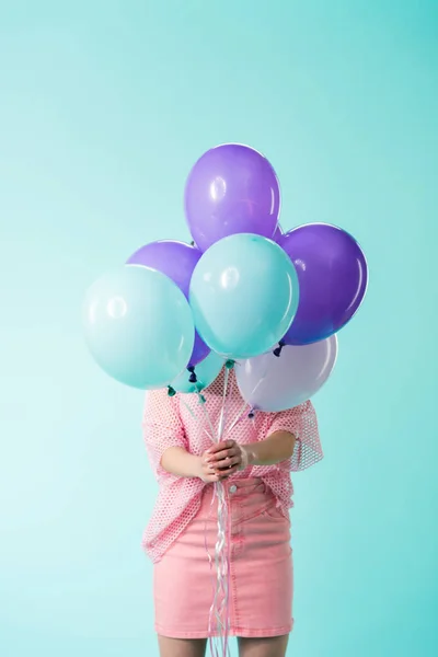 Chica en traje rosa sosteniendo globos en frente de la cara aislado en turquesa - foto de stock