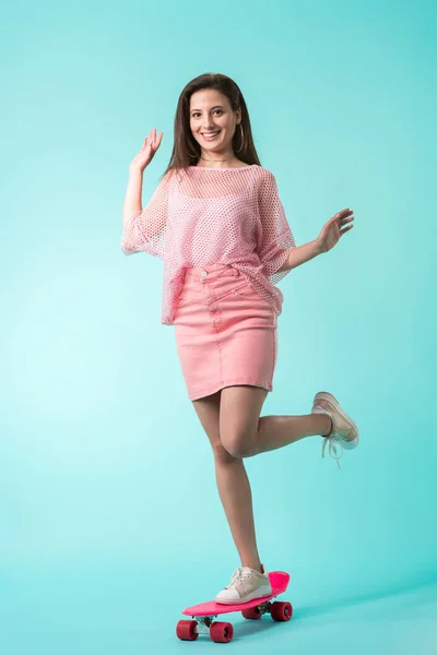 Щаслива дівчина в рожевому вбранні позує на дошці копійки на бірюзовому фоні — стокове фото