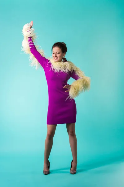 Happy party girl in purple dress with feathers dancing on turquoise background — Stock Photo