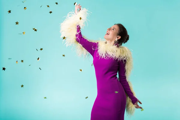 Happy party girl in purple dress with feathers dancing under falling confetti isolated on turquoise — Stock Photo