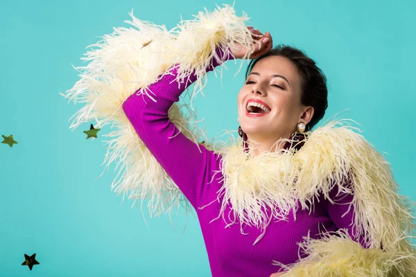 Happy party girl in purple dress with feathers under falling confetti isolated on turquoise — Stock Photo