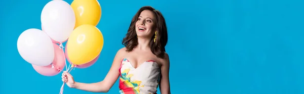 Panoramic short of happy elegant young woman in dress holding balloons isolated on blue — Stock Photo